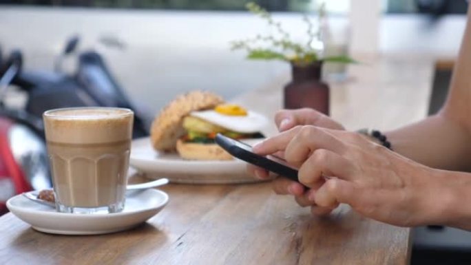 用智能手机拍摄女性双手的特写。一名妇女在吃素汉堡和植物性咖啡午餐的同时，在电话簿中寻找联系人进行直播
