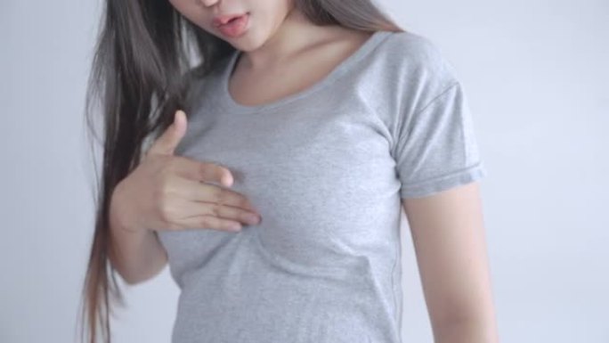 穿着灰色t恤的亚洲妇女正在自我检查是否患有乳腺癌。