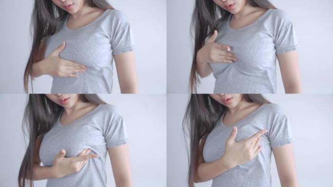 穿着灰色t恤的亚洲妇女正在自我检查是否患有乳腺癌。