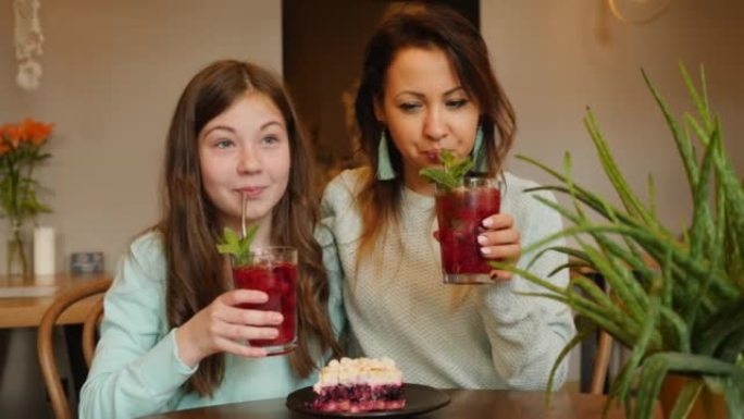 快乐的母亲和十几岁的女儿一起在舒适的餐厅庆祝生日，一起吃蛋糕，喝水果鸡尾酒，一起微笑