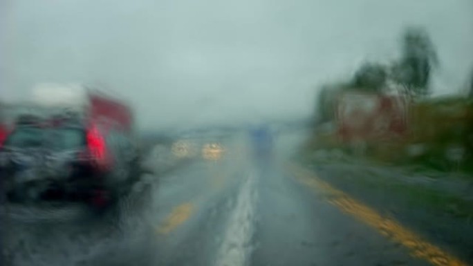 在雨中，在阴沉的天气里，在高速公路上行驶。高速公路上的超车被雨水模糊了。雨刮器擦拭汽车雨水浸湿的挡风