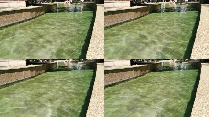 温泉公园里的温水流。溪床以石板装饰，底部有绿藻。远处的人们将脚留在溪流中。塞尔维亚尼斯卡·巴尼亚