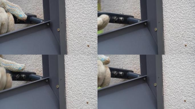 用铆钉钳将金属型材连接到围栏导轨上的人的手近距离拍摄。杂工用工具连接百叶窗栅栏的金属部件。