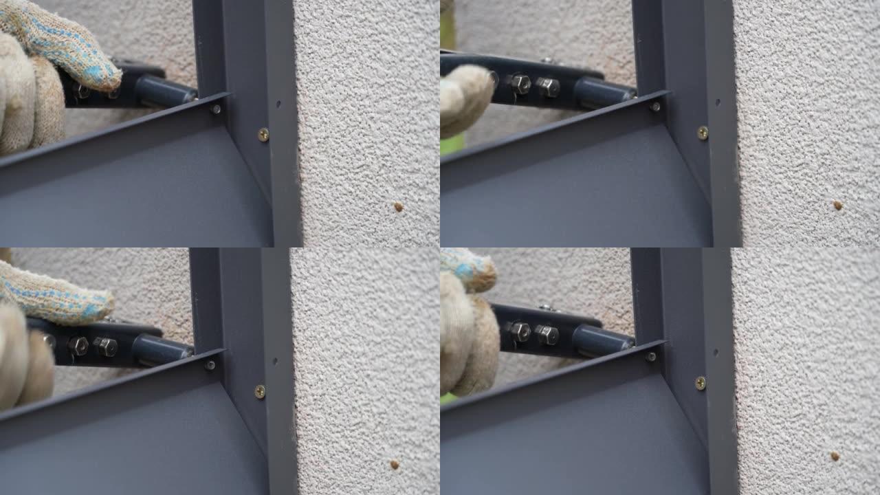 用铆钉钳将金属型材连接到围栏导轨上的人的手近距离拍摄。杂工用工具连接百叶窗栅栏的金属部件。