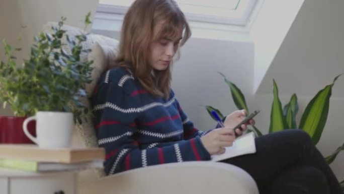 年轻女子在使用智能手机时写笔记