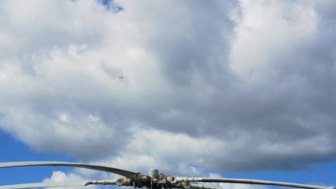 直升机的桨叶映衬着天空的云层，跳伞者在云层中飞行。伞兵在有直升机停机坪的机场上空的飞行。用降落伞进行