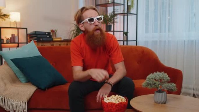 男人坐在沙发上吃爆米花，在家看有趣的电视连续剧，在线体育游戏