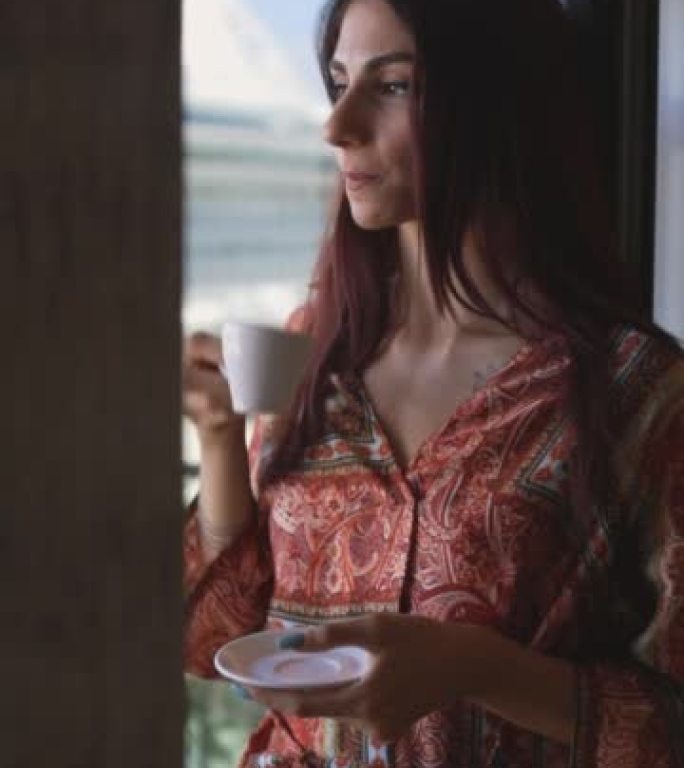 早上从窗前的杯子里喝咖啡的女孩的剪影，在窗边喝茶的女人的剪影，穿着睡衣的女人正在看大海和游轮的景色，