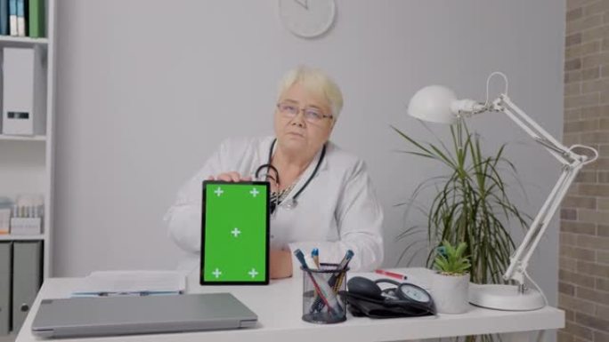 远程医疗概念女医生展示绿屏垂直平板电脑。