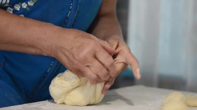 一位穿着蓝色连衣裙的老妇的手的特写镜头，捏住生面团形成面包。烹饪传统，家庭食谱。