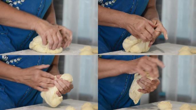 一位穿着蓝色连衣裙的老妇的手的特写镜头，捏住生面团形成面包。烹饪传统，家庭食谱。
