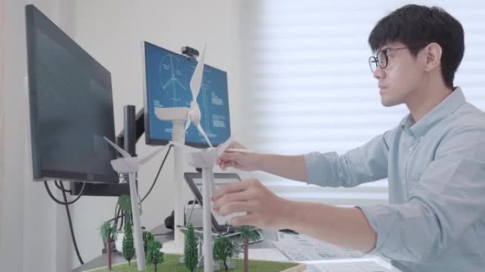 一名男性工程师与计算机全息增强现实3D屏幕一起工作的视频，内容涉及工作室中用于替代能源的风车和太阳能