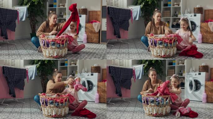 五岁的女孩和阿姨坐在地板上洗衣服。他们把脏衣服从篮子里拿出来，按颜色分类。他们交流，玩得开心。后面有