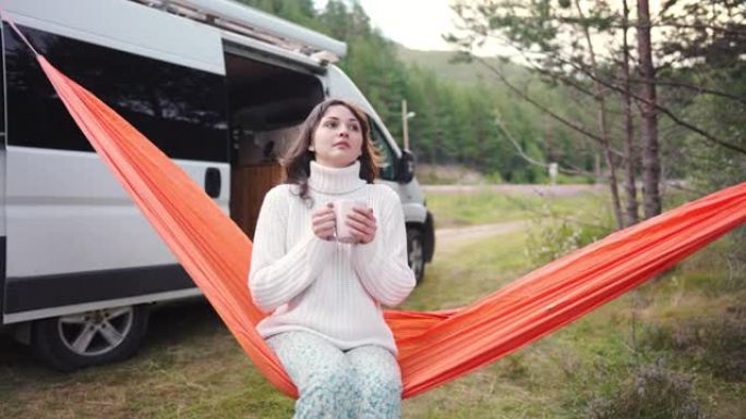 女人在露营车附近的吊床上休息时喝茶