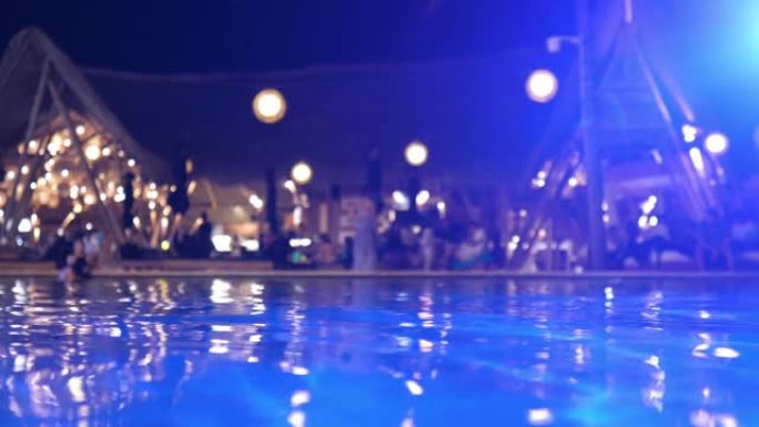晚上从水上到酒店泳池派对。夜灯从聚光灯和聚光灯在黑暗的水中倒影。在离家度假时24/7乐趣。