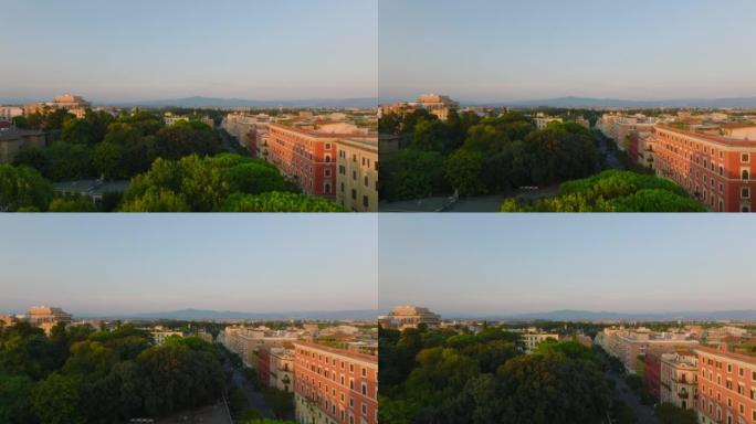 公园中生长的树木的鸟瞰图在低太阳照亮的公寓楼之间。向前飞行在市区上空。意大利罗马