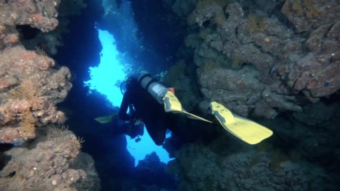 潜水员在水下洞穴中游泳，探索珊瑚礁，后视图跟踪拍摄