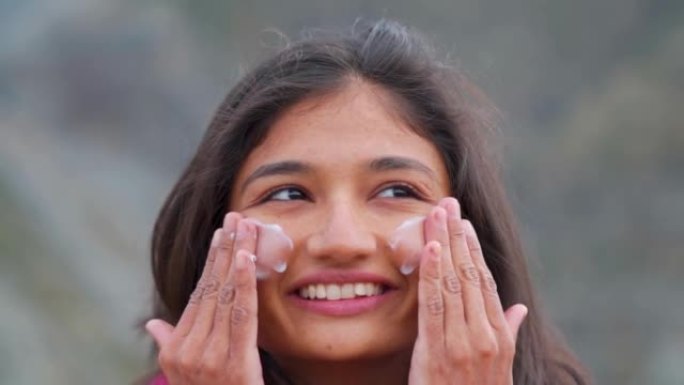 快乐微笑的印度少女站在户外时脸上涂抹防晒霜的肖像。保护皮肤免受晒黑。日常护肤程序。