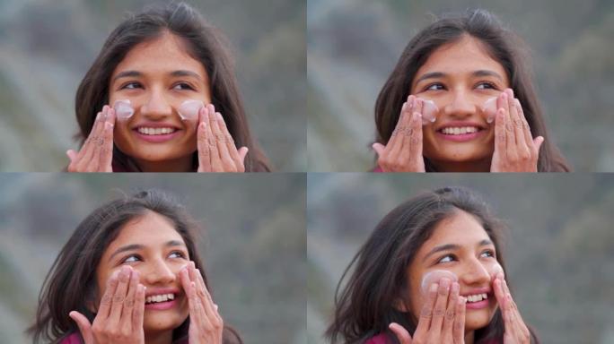快乐微笑的印度少女站在户外时脸上涂抹防晒霜的肖像。保护皮肤免受晒黑。日常护肤程序。
