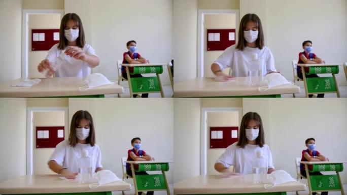 带口罩的女学生在教室里清洁手和带消毒抗菌凝胶的桌子