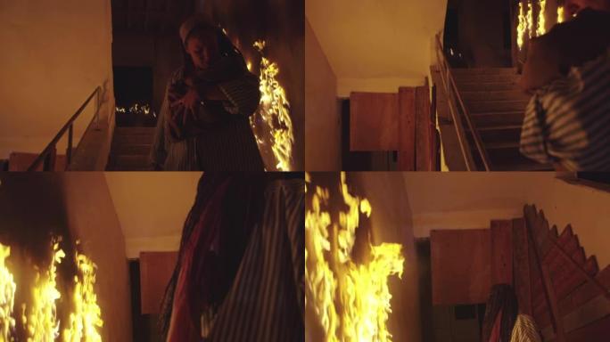 勇敢的消防员走下燃烧的建筑物的楼梯，将被拯救的女孩抱在怀里。开火，一名消防员在后台。