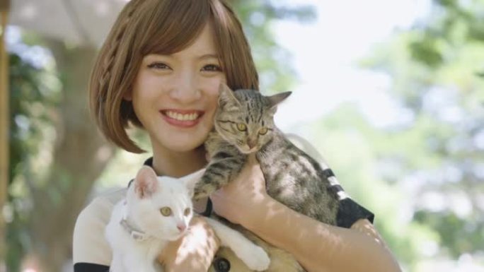 亚洲女人在花园里背着两只猫。