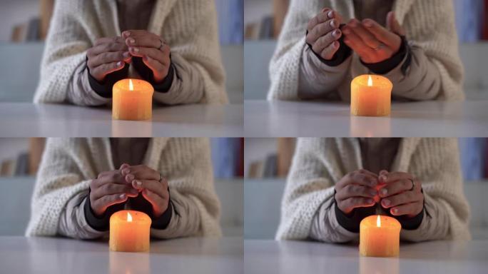 人的双手从燃烧的蜡烛中温暖起来。家里冬天不供暖的概念。停电、减载、能源危机。