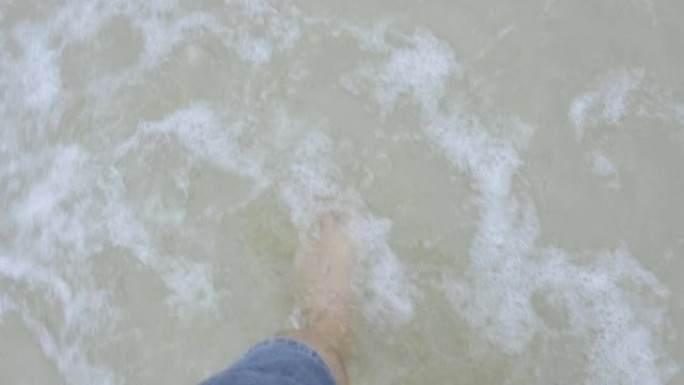 人的特写脚正独自从海滩走进清澈的大海。