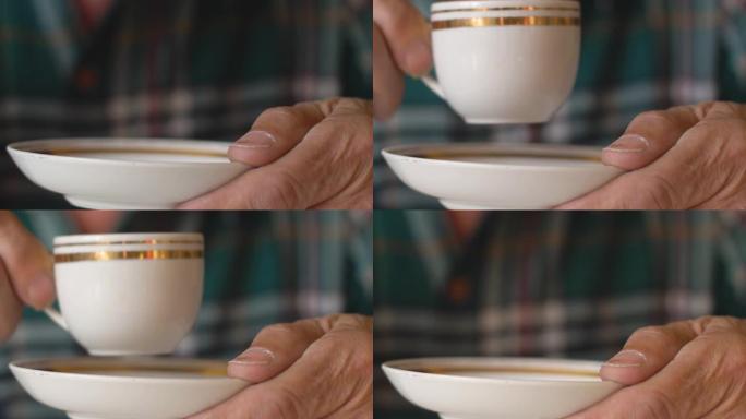 特写镜头在一个老人的手中，一个盘子和一杯咖啡。选择性聚焦。一个penisrner从杯子里喝一杯美味的