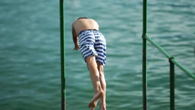 小男孩潜入水中。十几岁的孩子在码头码头以超慢动作坠入湖中。孩子们在暑假期间玩得开心