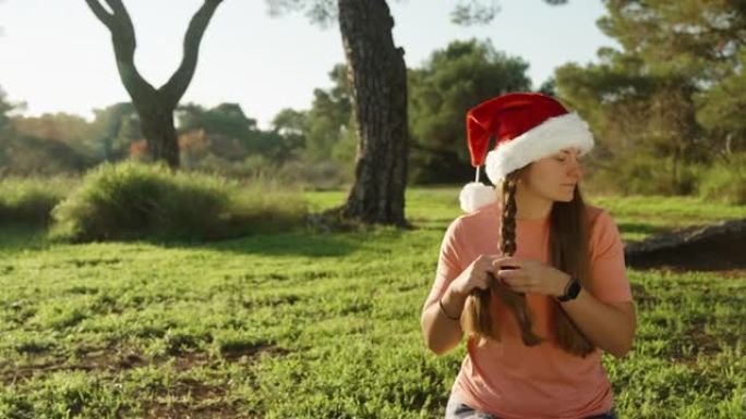 我把头发编成辫子，一个戴着红色圣诞老人帽子的女孩。圣诞节在树林里瑜伽。阳光明媚温暖的圣诞节。