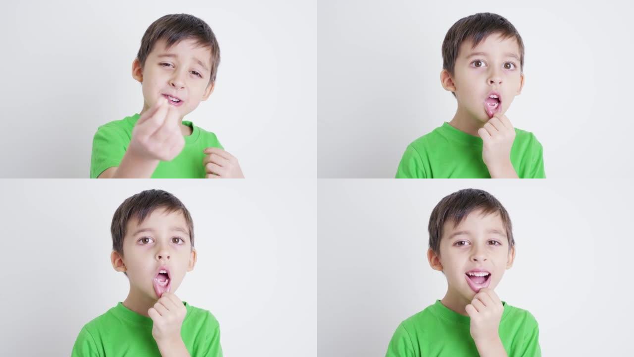 穿着绿色t恤的男孩孩子露出没有正面乳牙的嘴，并在镜头前露出牙齿，站在房间的白色背景上。