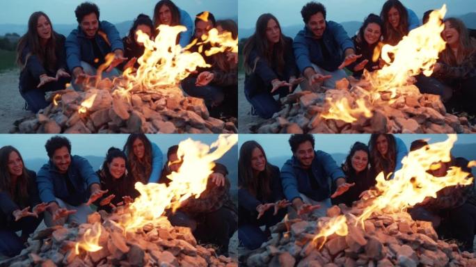 一群朋友在篝火晚会上一起玩乐-友谊生活方式概念与快乐的人旅行者在黄昏夜晚的篝火旁让自己温暖
