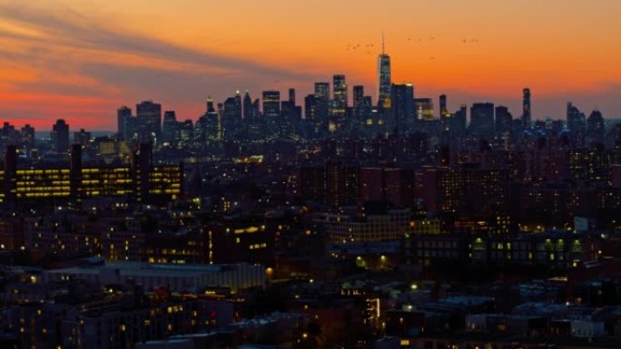 曼哈顿市区和自由塔上空的戏剧性天空在夜晚照亮。鸟群在飞翔。日落时分，可以看到布鲁克林住宅区的远景。静
