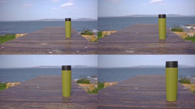 一个绿色的保温杯站在海洋背景下的木桌上