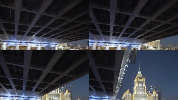 莫斯科以斯大林主义风格设计的带照明摩天大楼的深夜城市景观。行动。在桥下航行，在深蓝色的夜空背景下展现