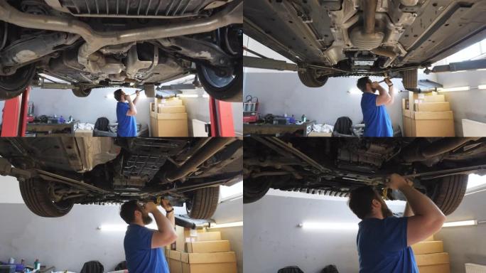 摄像机在车间用特殊工具转移到专业的大胡子汽车修理工。穿着制服的年轻修理工在车库的起重车辆下面工作。汽