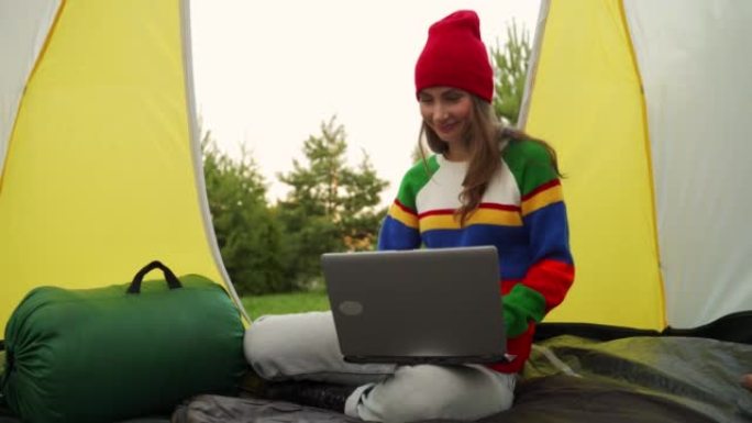 戴着红色帽子的女人坐在帐篷里在笔记本电脑上工作