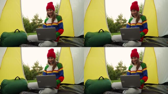 戴着红色帽子的女人坐在帐篷里在笔记本电脑上工作