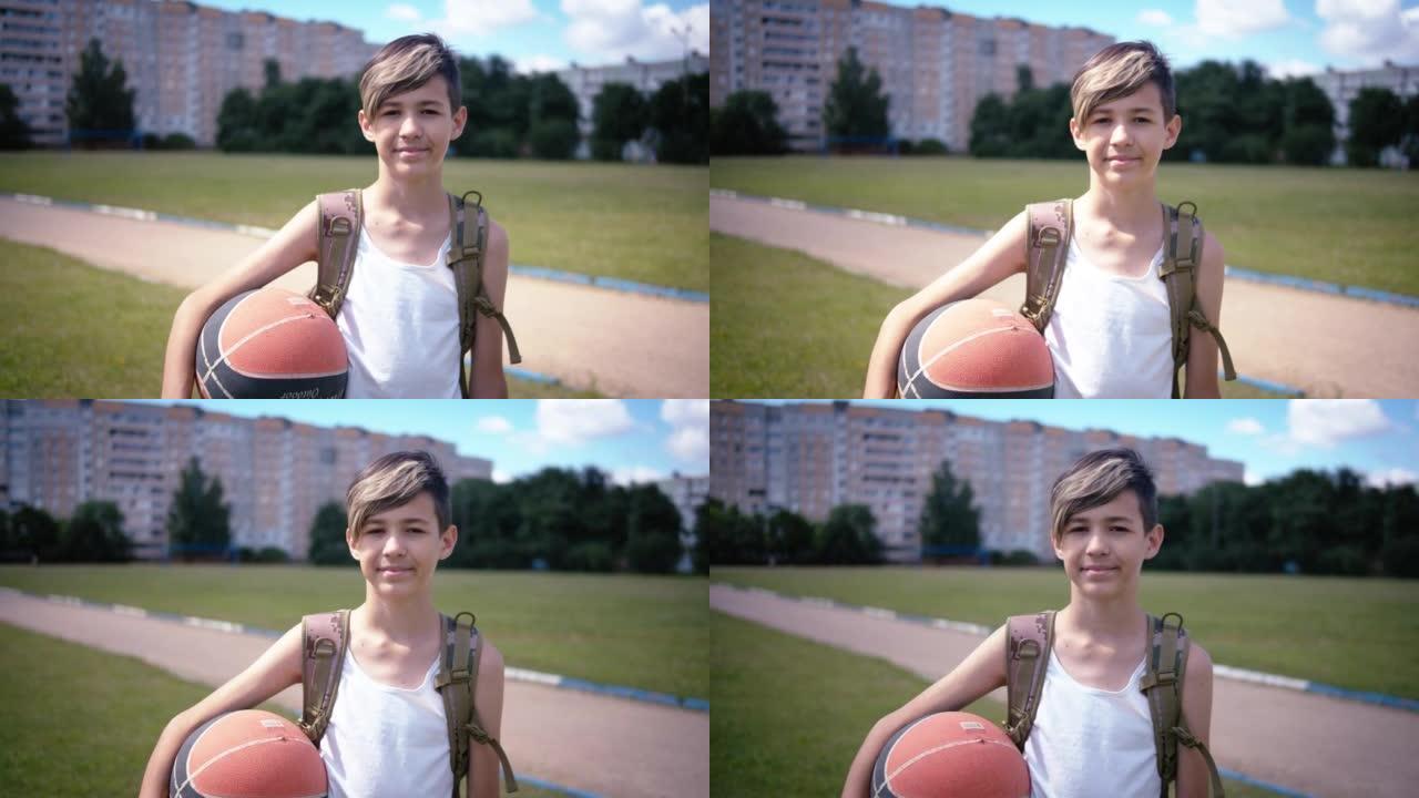 十几岁的男孩带着一个篮子的球看着相机，微笑着，在夏天阳光明媚的日子里，移动相机