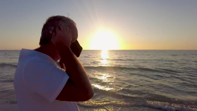 中年男子在海滩上看着金色的日落戴上口罩。美国佛罗里达州克利尔沃特市暑假时，年轻的白人男子向大海望去。