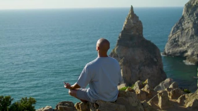 瑜伽男子在金色的阳光下在美丽的海崖边练习冥想。