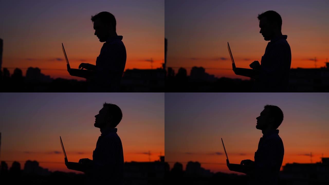 日落时户外使用笔记本电脑的显影剂男性剪影，工作，4K