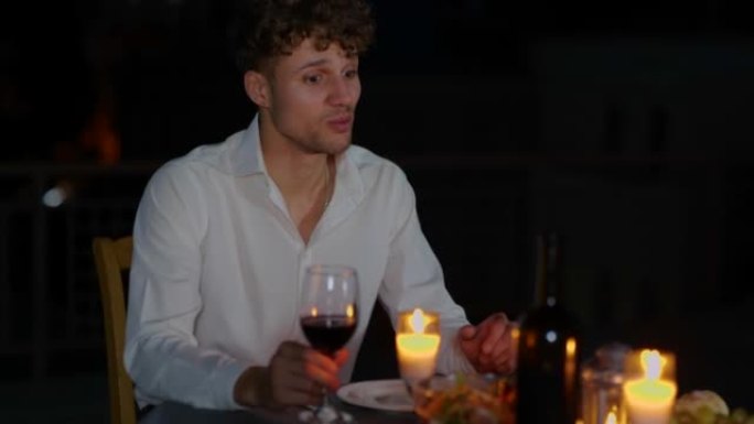 英俊的年轻男性坐在餐桌旁，拿着蜡烛在浪漫的晚餐上，女朋友喝着酒说话。快乐的男人晚上和心爱的女人浪漫约