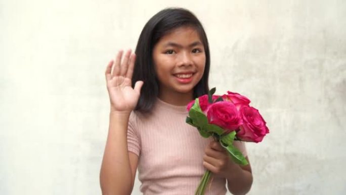 亚洲少女手持一束粉红色的花朵，摆姿势招手示意，白色的旧墙壁背景