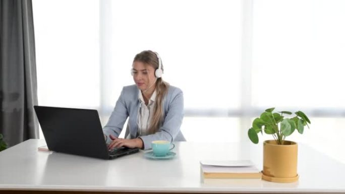 年轻的女商人在办公室里用笔记本电脑听耳机上的音乐。女商人以轻松的旋律享受工作时间。