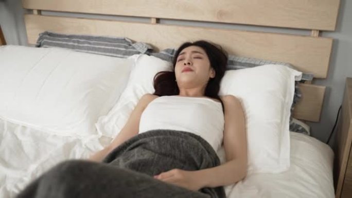 被毯子覆盖的沮丧的亚洲女孩醒着躺在卧室的床上，不想早上在家起床上班。