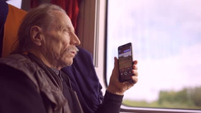 老人乘火车旅行，并使用智能手机通过窗户拍照