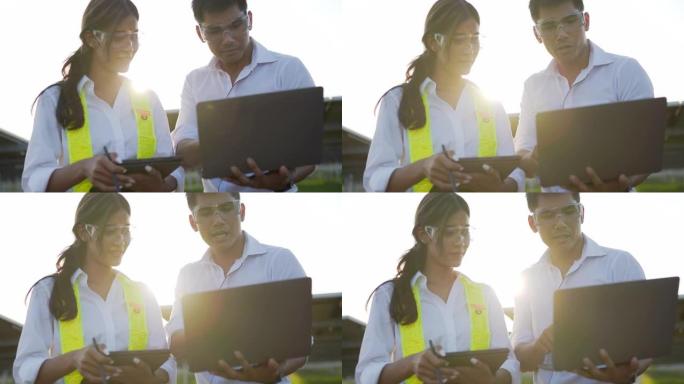 背光镜头，年轻的工程师男女戴着保护眼镜站立并使用笔记本电脑和平板电脑在太阳能站工作