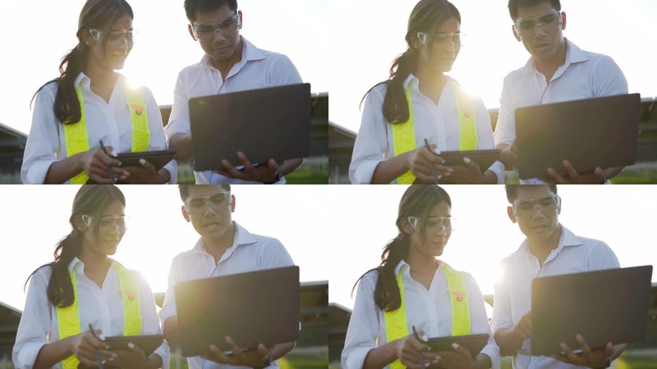 背光镜头，年轻的工程师男女戴着保护眼镜站立并使用笔记本电脑和平板电脑在太阳能站工作
